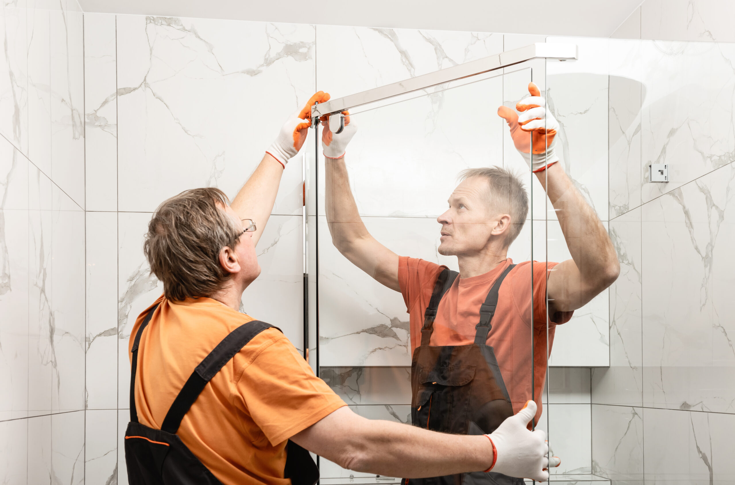 Workers are installing glass door of the shower enclosure.