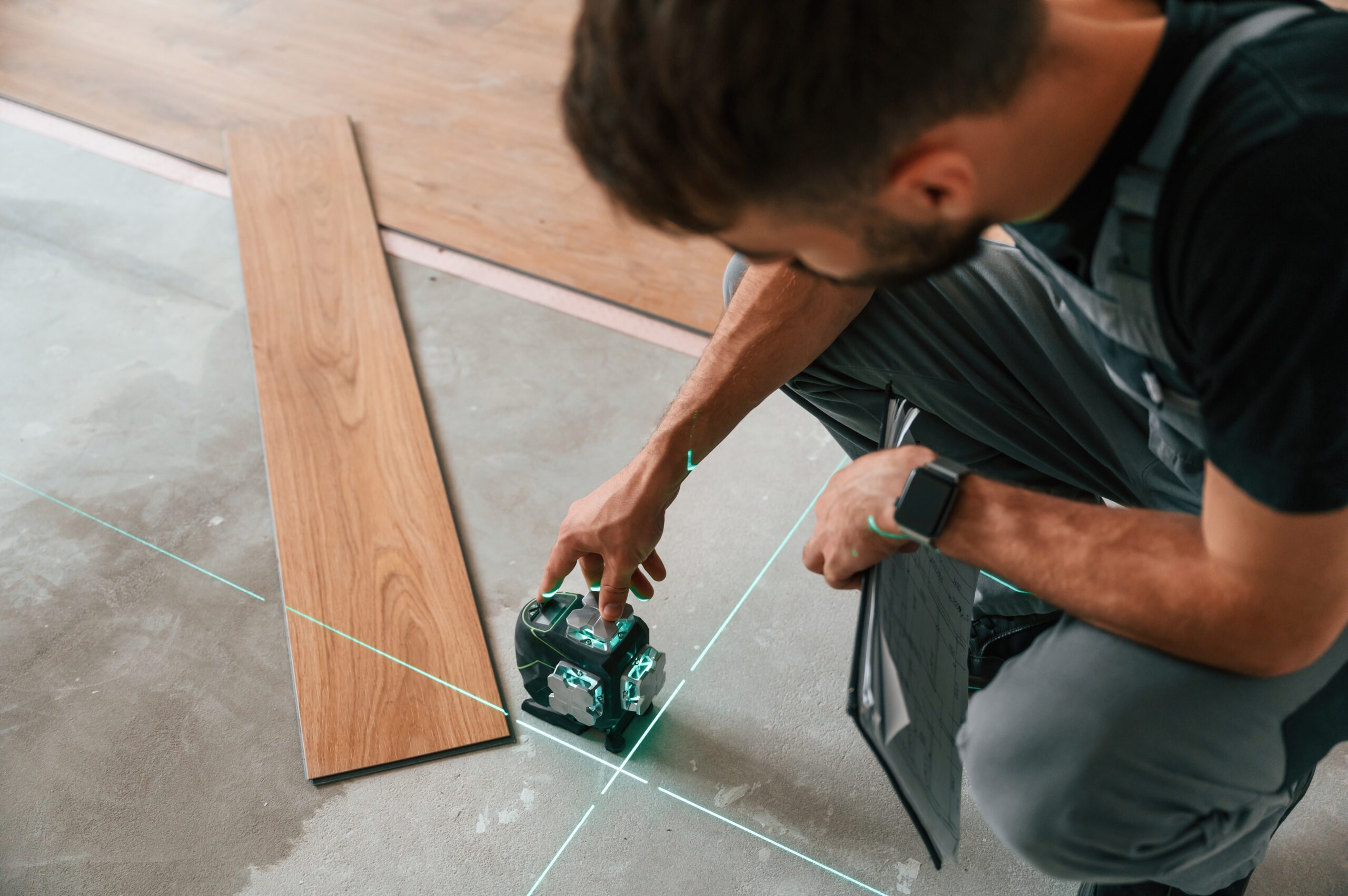 Using the device that shows straight lines by laser. Man is installing new laminated wooden floor.