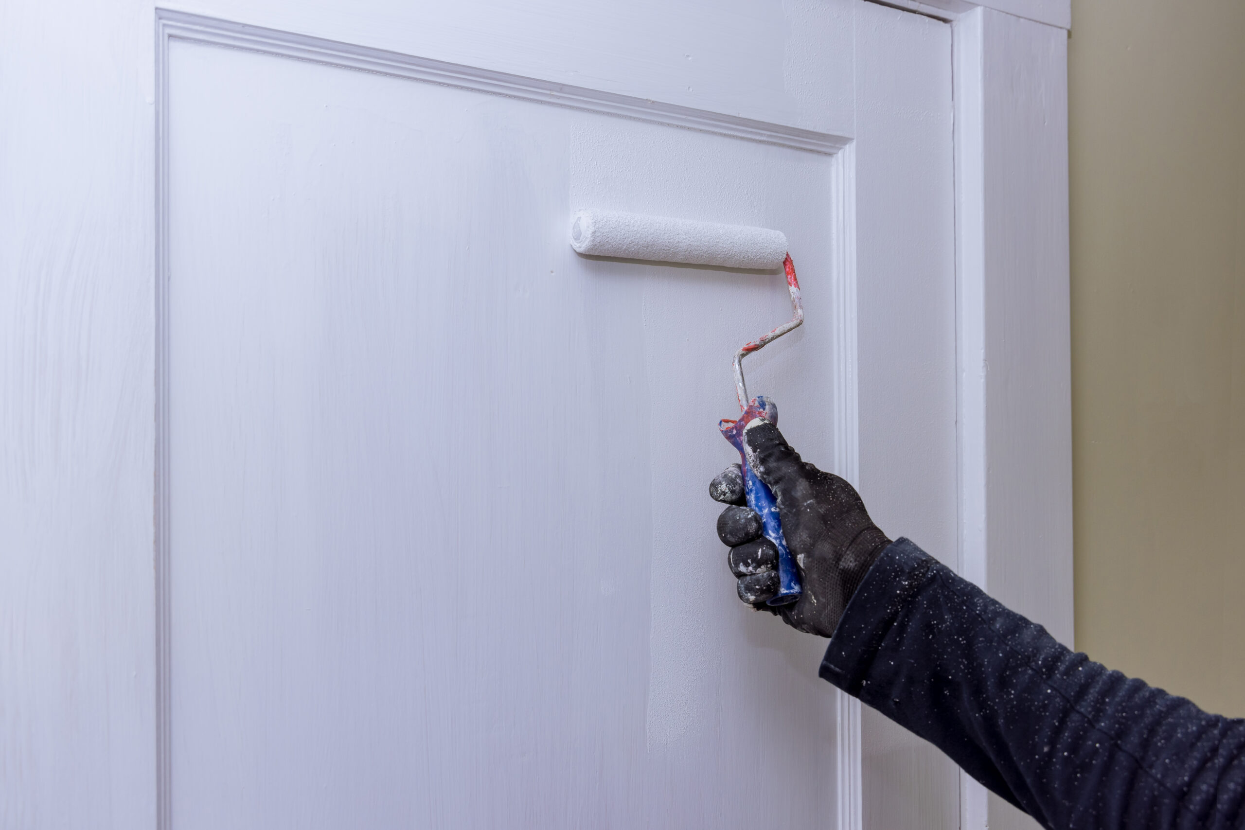 Close up of painter hands with gloves painting the door frame using hand roller on worker home restoration